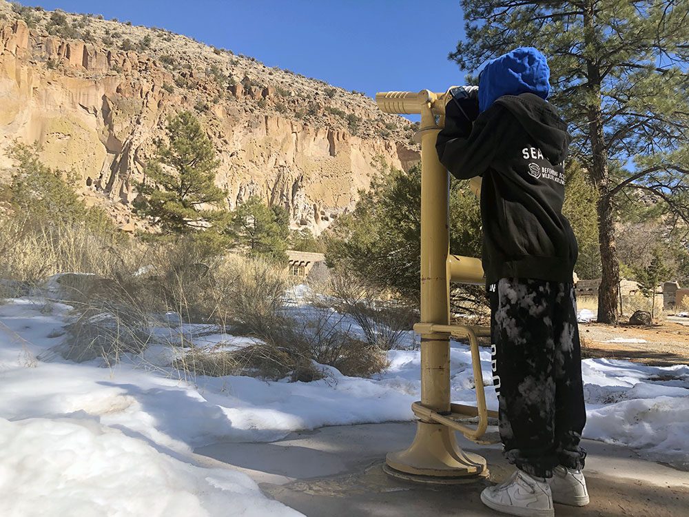 young kid looking into the telescope at snowy bandelier trail in santa fe new mexico