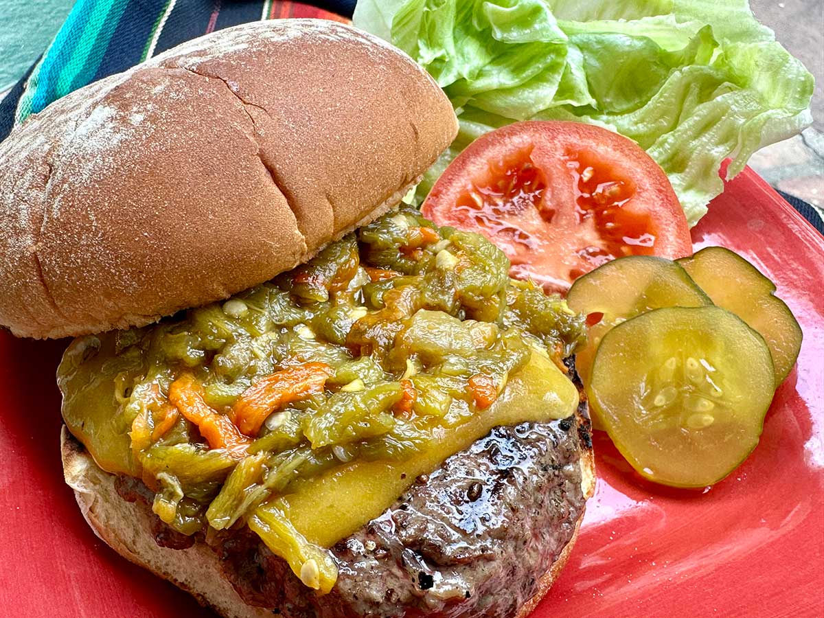 Green chile cheeseburger with lettuce, tomato, and pickles on the side