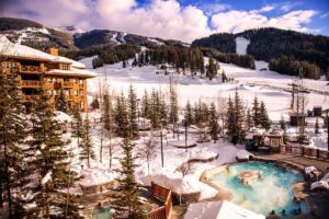 Panorama base area shows buildings in foreground, large hot springs, and snow-covered mountains.