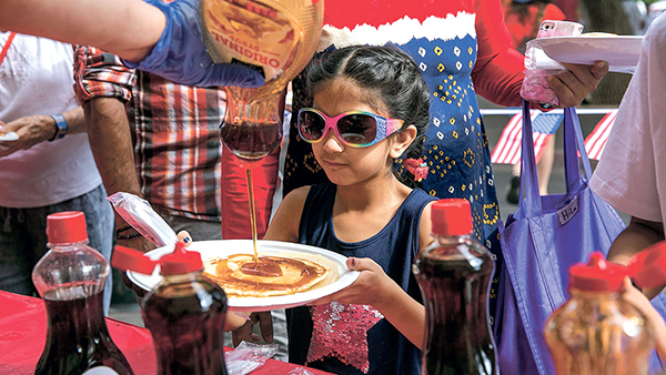 little girl in sunglasses getting syrup on her pancakes 